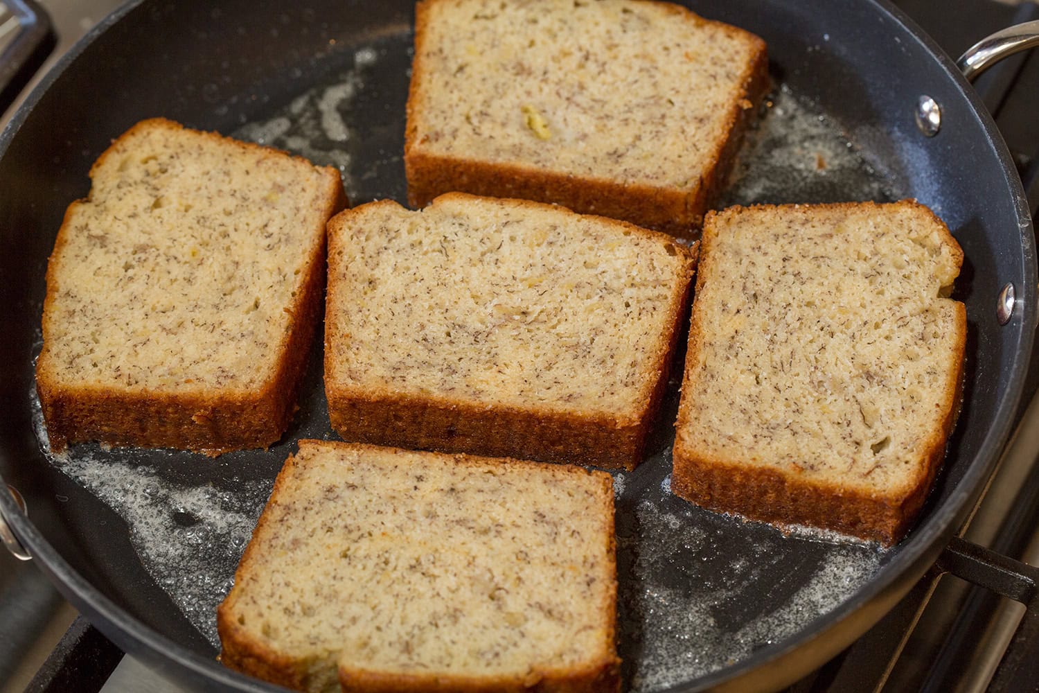 Banana bread slices frying in butter in a large non-stick skillet on first side.