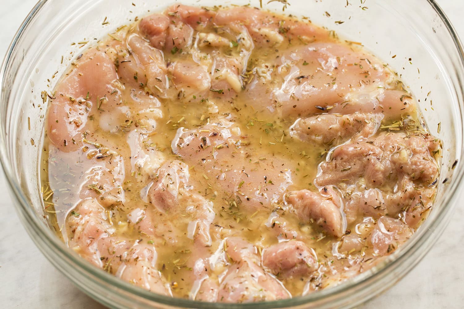 Chicken thighs shown soaking in marinade in glass mixing bowl.