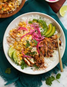 Overhead image of street corn and chicken rice bowl on a blue cloth on a marble surface.
