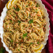 Overhead photo of tuna pasta made with spaghetti noodles, canned tuna, capers, and sun dried tomatoes in a scalloped white bowl.