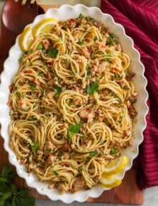 Overhead photo of tuna pasta made with spaghetti noodles, canned tuna, capers, and sun dried tomatoes in a scalloped white bowl.