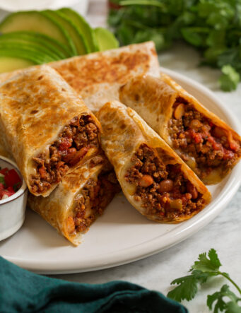 Easy homemade ground beef burritos shown aligned on a platter and cut into halves to show filling.
