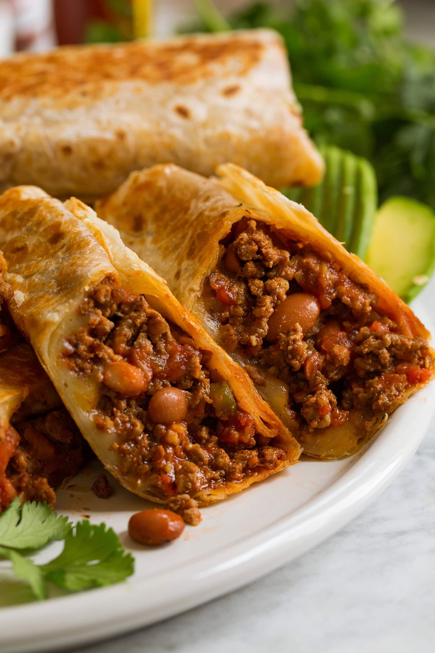 Close up photo of ground beef and bean burritos with cheese, sliced in half exposing filling.