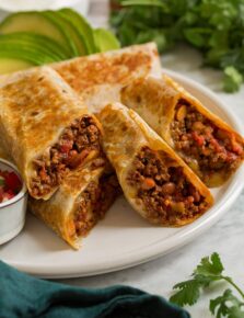 Easy homemade ground beef burritos shown aligned on a platter and cut into halves to show filling.