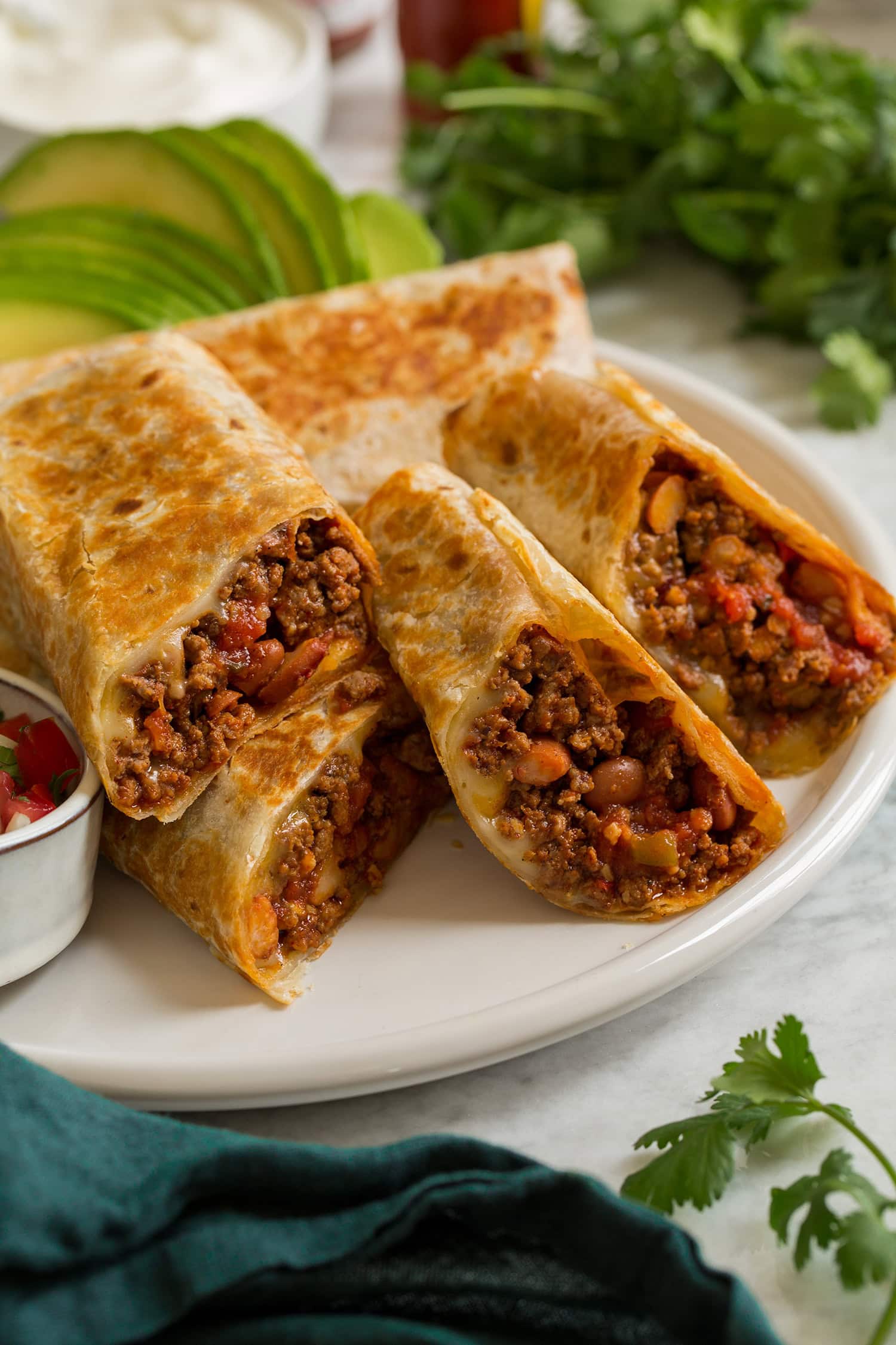 Easy Beef Burritos Easy homemade ground beef burritos shown aligned on a platter and cut into halves to show filling.