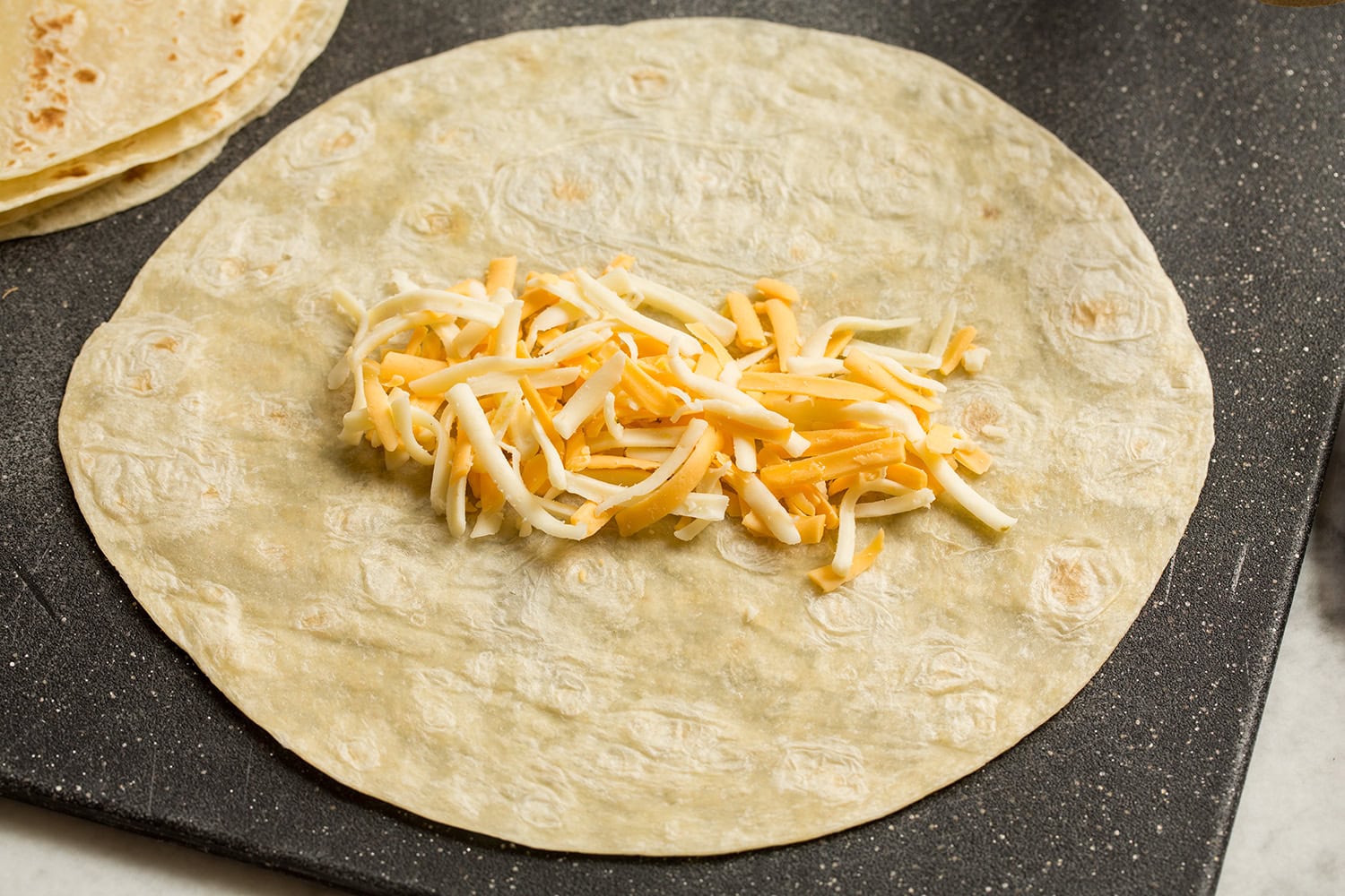 Easy Beef Burritos Showing how to assemble a burrito starting with a cheese layer in a row in center of tortillas.