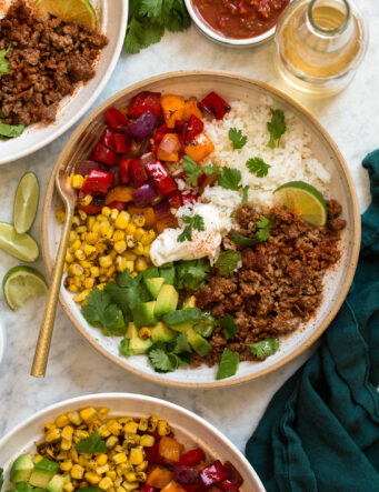 Overhead photo of ground beef fajita bowls with rice, bell peppers, avocado, and corn.