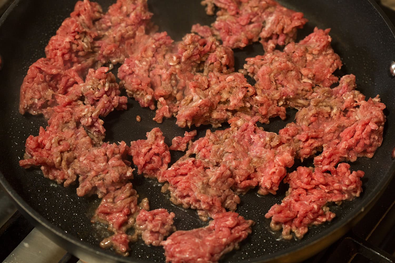 Raw ground beef in crumbles in skillet.
