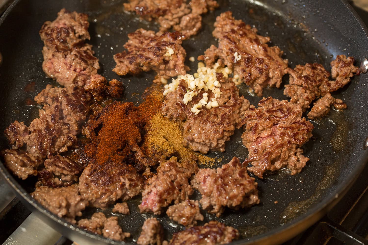 Browned ground beef turned over with garlic and spices on top in skillet.