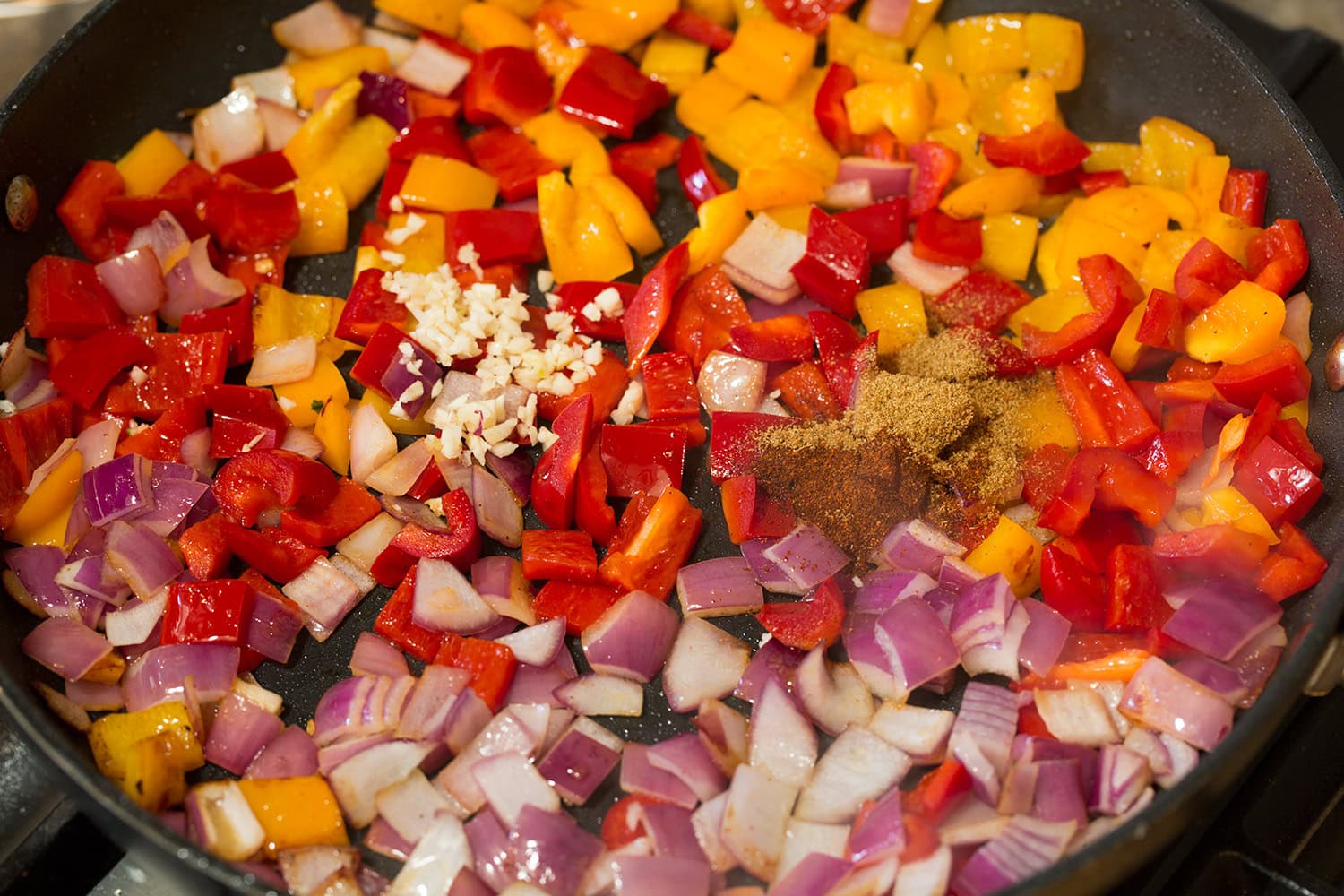 Bell peppers, red onion garlic and spices in a skillet sauteeing.