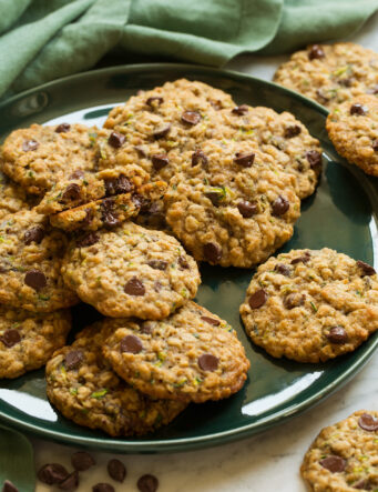 Large green plate with zucchini oatmeal chocolate chip cookies layered on it.