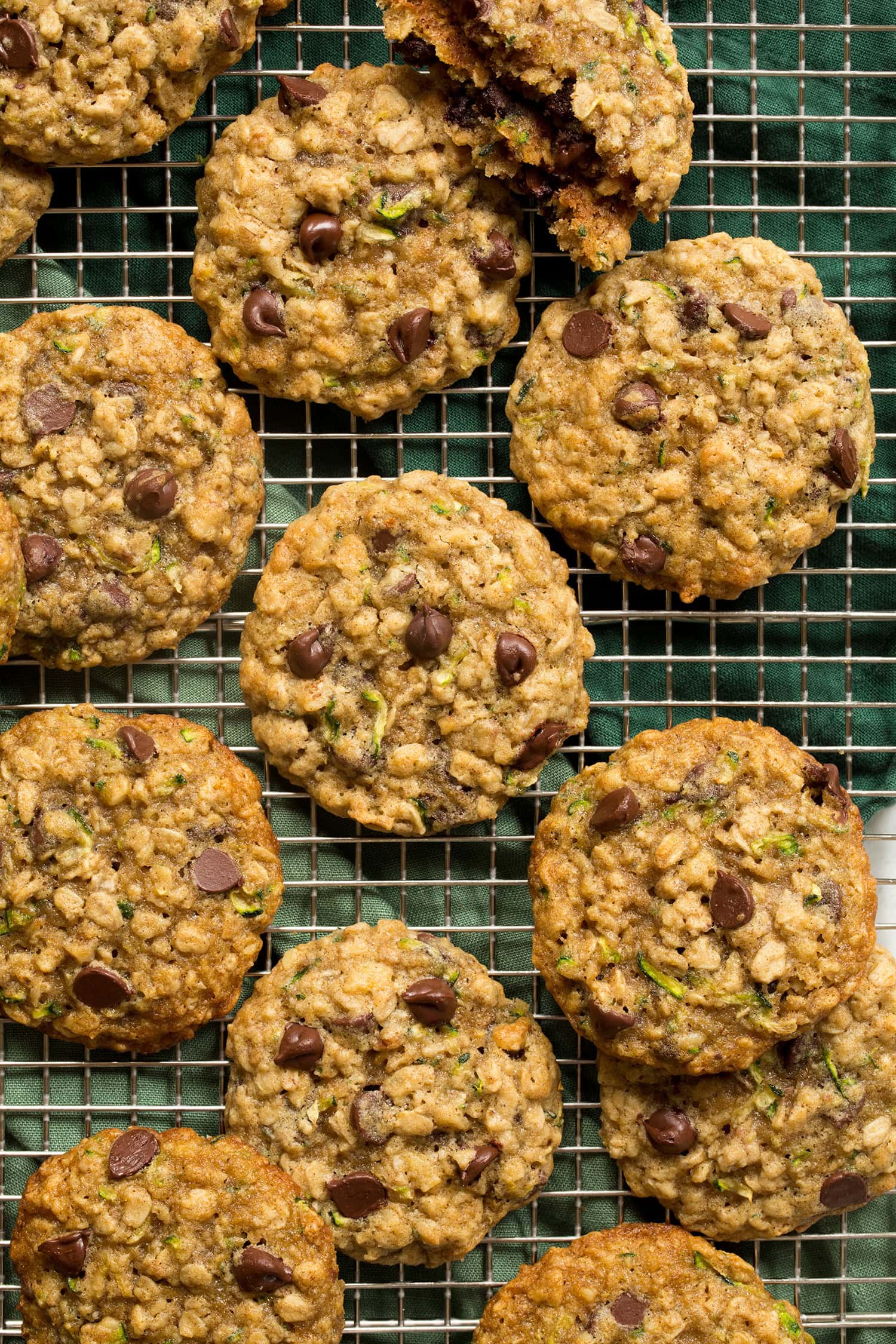 Close up overhead photo of zucchini oat chocolate chip cookies on a wire cooling rack over a green cloth. Shows texture of cookies.